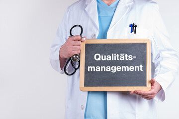 Arzt mit einer Tafel auf der Qualitätsmanagement steht.