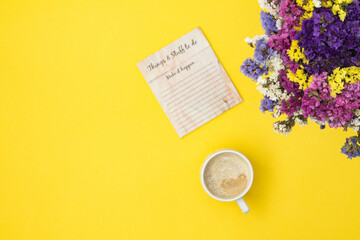 Cup of coffee, notebook, and bouquet of flowers on yellow background. Business or national coffee day concept. 
