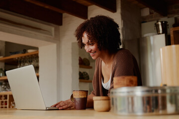Fototapeta na wymiar Young biracial woman smiling while working from home on laptop in kitchen