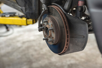 The brake drum of the front axle of a car lifted above the ground with the disc caliper and brake...