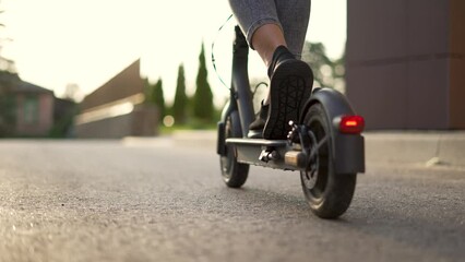 Girl rides an electric scooter. Child travel cheerfully. Empty city street. Legs on an electric scooter. Girl travel on scooter. Child on deserted street. Electric scooter close up. City travel girl