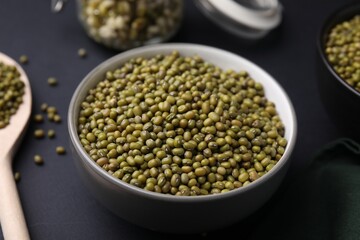 Different dishware with green mung beans on black background, closeup