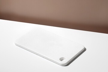 White empty marble board on white table. Blank, still life scene, beige wall, background with plate.
