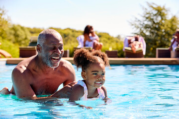 Grandfather Teaching Granddaughter To Swim In Outdoor Pool On Holiday