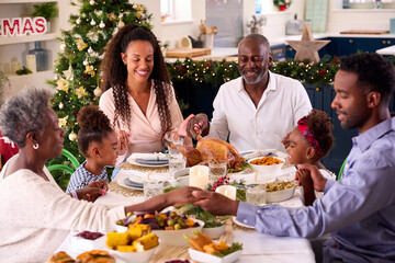 Multi-Generation Family Celebrating Christmas At Home Saying Prayer Before Eating Meal Together