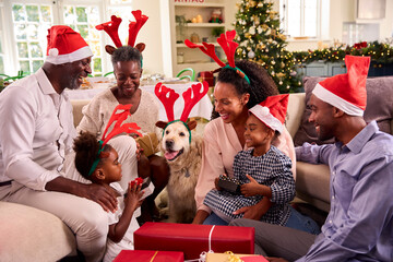 Multi-Generation Family Celebrate Christmas At Home Wearing Santa Hats And Antlers Opening Presents