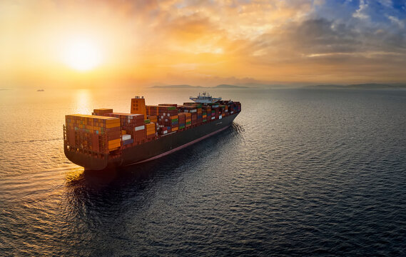 Aerial view of a large, heavy loaded container cargo ship sailing over calm sea into the sunset