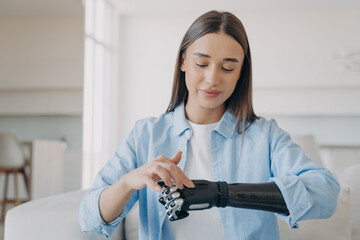 Pretty disabled girl adjusting her bionic prosthetic arm touching sensory panel of artificial hand