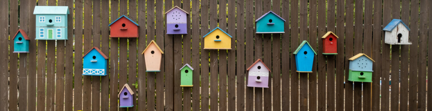 Multi-colored bird houses are located on a wooden fence as decoration. Housing for birds as an element of decor and stylish fun decoration. Background, texture