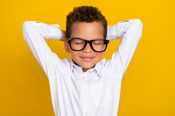 Portrait of cute dreamy boy stylish white clothes glasses hold hand behind head relax after school week isolated on yellow color background