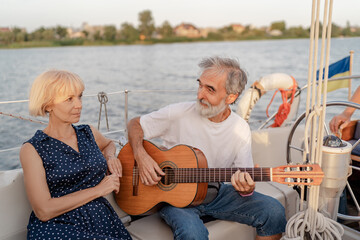 Fototapeta na wymiar Romantic vacation and luxury travel. Senior loving couple sitting on the yacht deck. Sailing the river.