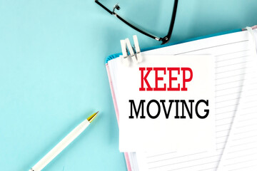 KEEP MOVING text on a sticky on notebook with pen and glasses , blue background
