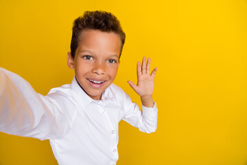 Photo of cute funny boy remote distance lesson hand wave classmates friends say hi empty space isolated on yellow color background