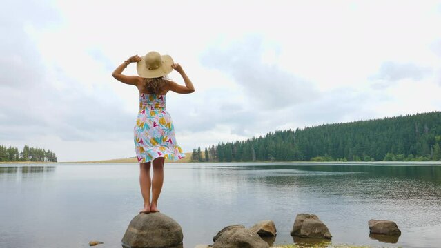 woman wearing dress and hat looking at beautiful lake and forest