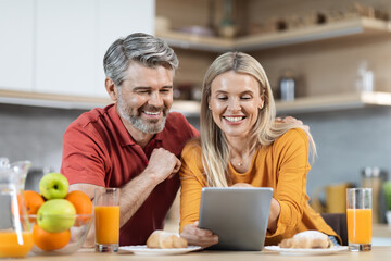 Loving couple enjoying healthy breakfast, using digital tablet