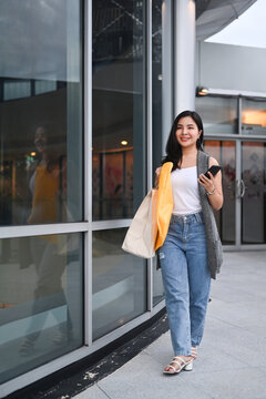 Stylish young woman with shopping bags walking outside shopping mall in the evening