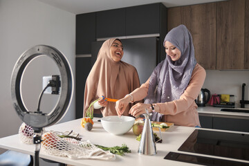 Two muslim food vloggers laughing while preparing a salad at modern kitchen.