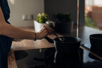 Close up of cropped unrecognizable woman hands cooking food in frying pan on induction cooker, stove with ceramic top