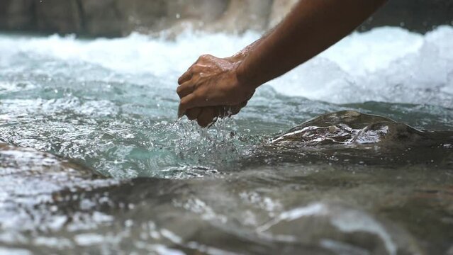 Unrecognizable hiker washing hands in mountain river with clear cool water. Guy standing among river with fast stream and refreshing. Male tourist during his travelling. Slow mo Low view Close up