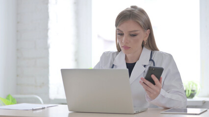 Lady Doctor using Smartphone while using Laptop in Clinic