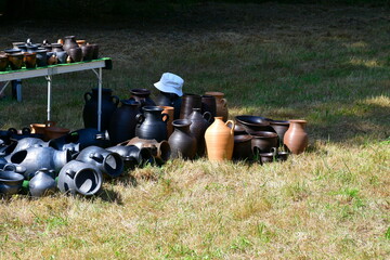 A close up on a set of colorful clay pots, bowls, and other containers standing on display and being available for purchase seen on a local oddity fair organized on a Polish countryside in summer