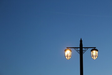 Fototapeta na wymiar Golden street lamps at night against a darkening evening sky with copy space. Concept background for nighttime shows, dusk, evening at the waterfront, relax, getaway vacation (Sidmouth, UK)