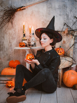 woman at a Halloween costume party in the image of a witch makeup on the background of burning candles and pumpkin