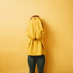 redhead woman hiding her face behind her arms, copyspace against yellow background