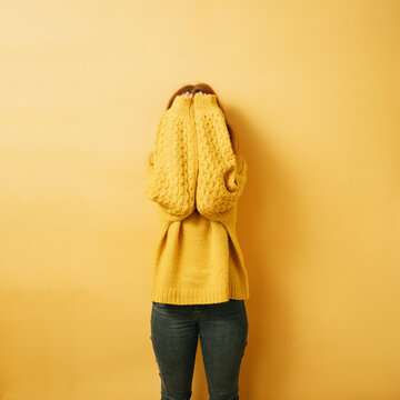 redhead woman hiding her face behind her arms, copyspace against yellow background