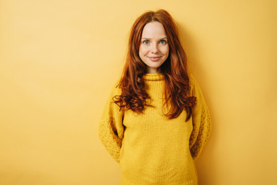 sensitive redhead woman with yellow sweater looks into camera, copyspace against yellow background