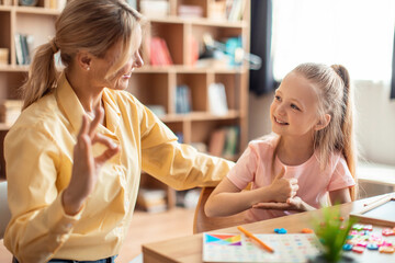 Positive teacher making hand gesture practice nonverbal talk with girl child, tutor learn sign...
