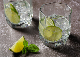 Classic Gin and tonic or Tom Collins or Gin Fizz alcoholic cocktail with Gin, tonic, ice and lime wedge on a grey background