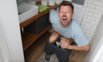 Man suffering from hemorrhoids screams on toilet in toilet - obrazy, fototapety, plakaty