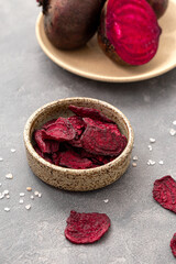 Beetroot chips in a bowl on a gray background. Healthy vegetable chips, snack for vegetarians, vertical photo