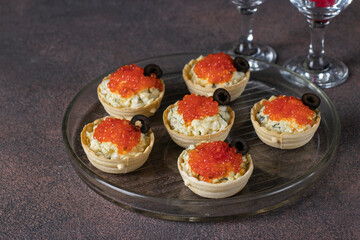 Festive tartlets with red caviar, egg and melted cheese, decorated with black olives