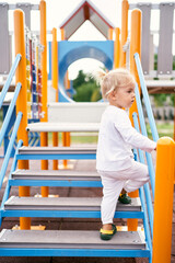 Little girl climbs the stairs to the colorful slide holding on to the handrail. High quality photo