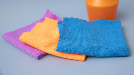 On a blue background, there are microfiber cleaning cloths of different colors laid out on the back of an orange pulevizer