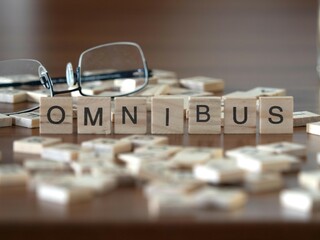 omnibus word or concept represented by wooden letter tiles on a wooden table with glasses and a book