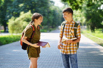 portrait of students in a city park, teenage schoolchildren a boy and a girl are standing on the path and discussing lessons, reading a book and talking