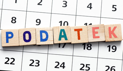 "Podatek" translated as "Tax"  word composed of wooden letters on a piece of paper of the calendar. It's time to settle accounts with the office.
