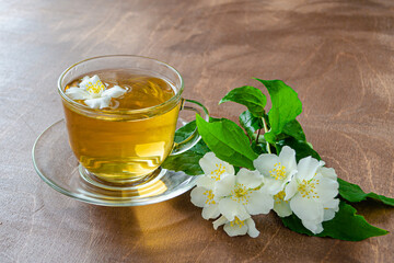 cup of jasmine tea and tea leaves on a wooden table next to jasmine sprigs with leaves and flowers, herbal tea healing diet