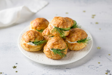Cheese profiteroles with cream cheese, cucumber and herbs, gougeres, traditional French pastries, in a white plate on a light gray background