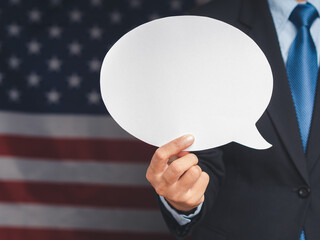 Close-up of a hand businessman holding a blank white speech bubble while standing on the American flag background