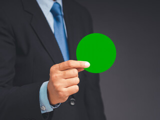 Close-up of hand businessman in a suit holding a blank green circle paper while standing on a gray background