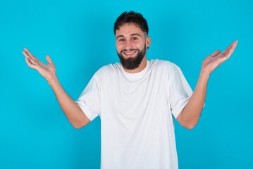bearded caucasian man wearing white T-shirt over blue background raising hands up, having eyes full of happiness rejoicing his great achievements. Achievement, success concept.