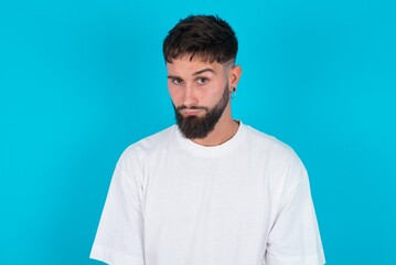 Fototapeta premium bearded caucasian man wearing white T-shirt over blue background frowning his eyebrows being displeased with something.