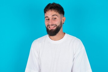 Obraz premium Oops! Portrait of bearded caucasian man wearing white T-shirt over blue background clenches teeth and looks confusedly aside, realizes her bad mistake,