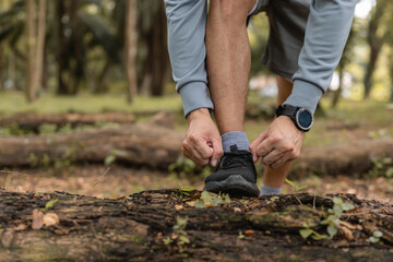 Fototapeta premium Man tying running shoes on path forest, preparing for a run exercise workout outdoor.