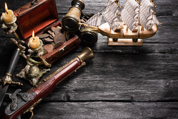 Obraz na płótnie Canvas Pirate concept background. Treasure chest with coins, musket gun, dagger, binoculars and ship on black wooden table background with copy space.
