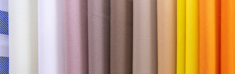 Fototapeta premium Samples of colored gabardine fabrics in selective focus. A large assortment of high-quality and fashionable fabrics, a choice of textiles in the fabric store.